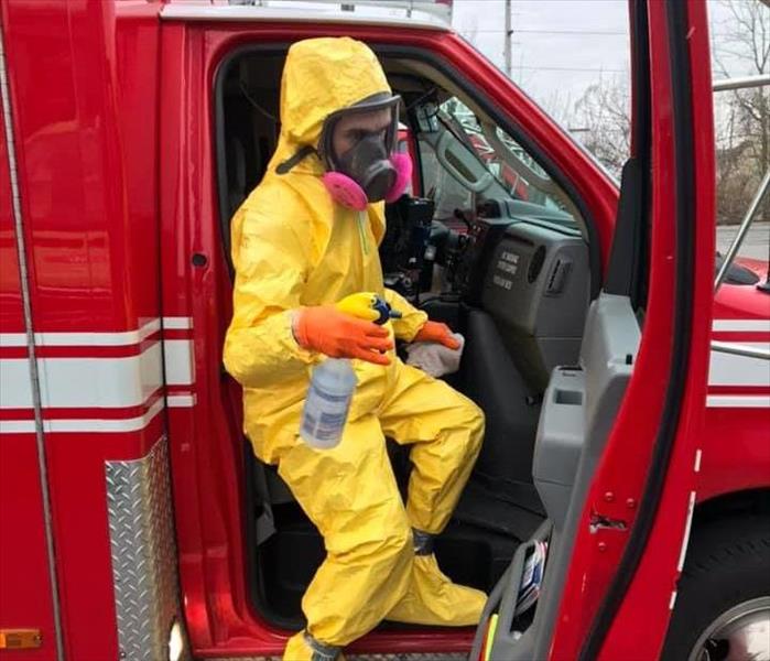 SERVPRO tech in yellow PPE cleaning red Kingston ambulance