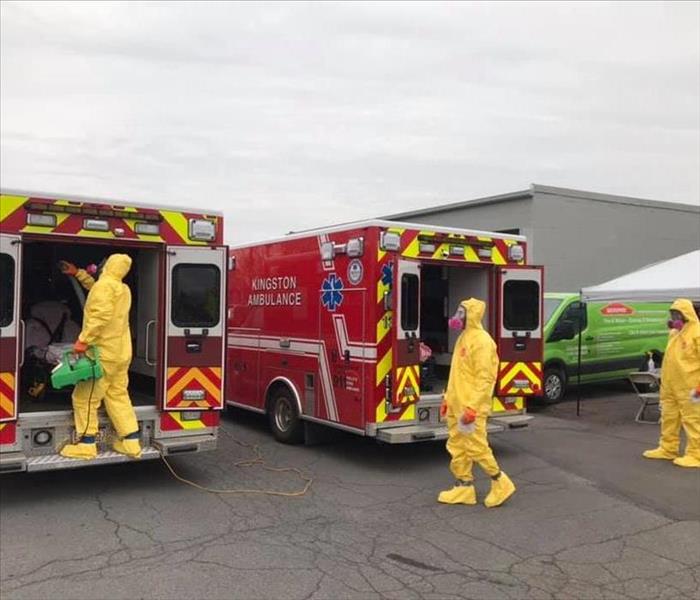 Three SERVPRO techs cleaning two red Kingston Ambulances 