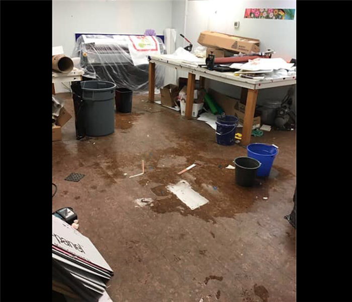 White room with brown floors and water on floor. Store equipment in background