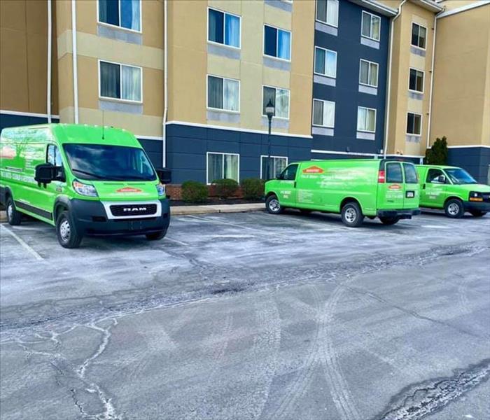 Three green SERVPRO trucks in front of hotel