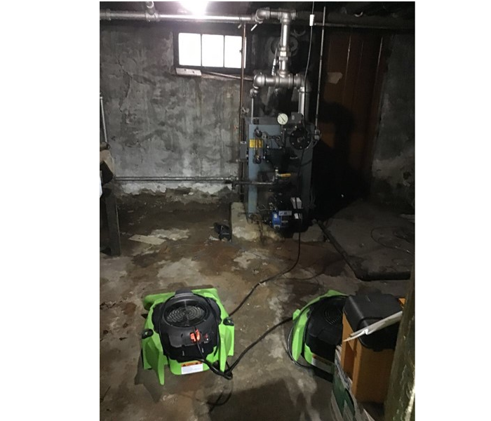 concrete basement with green SERVPRO fans drying out the water damage near the water heater