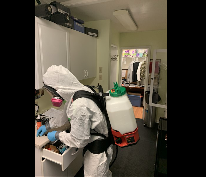 SERVPRO technician in white PPE disinfecting cabinets