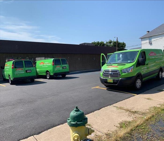 Three green SERVPRO trucks in parking lot of commercial building