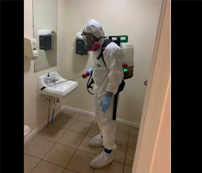 Technician in white PPE fogging restroom 